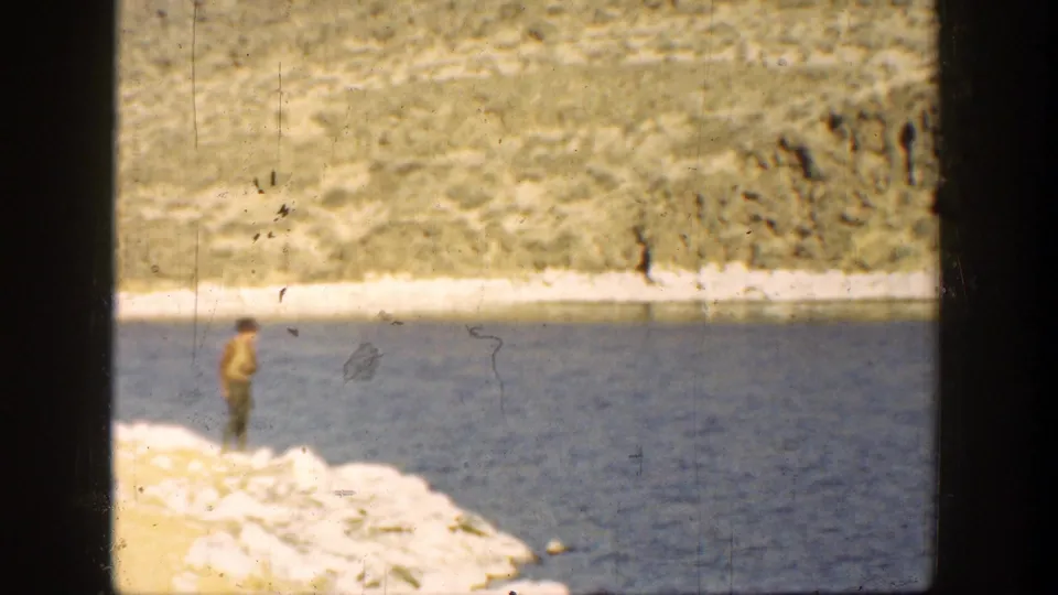 Soft 1936 California home-movie frame showing the man on the shore, framed by dark film borders and a sunlit river landscape.