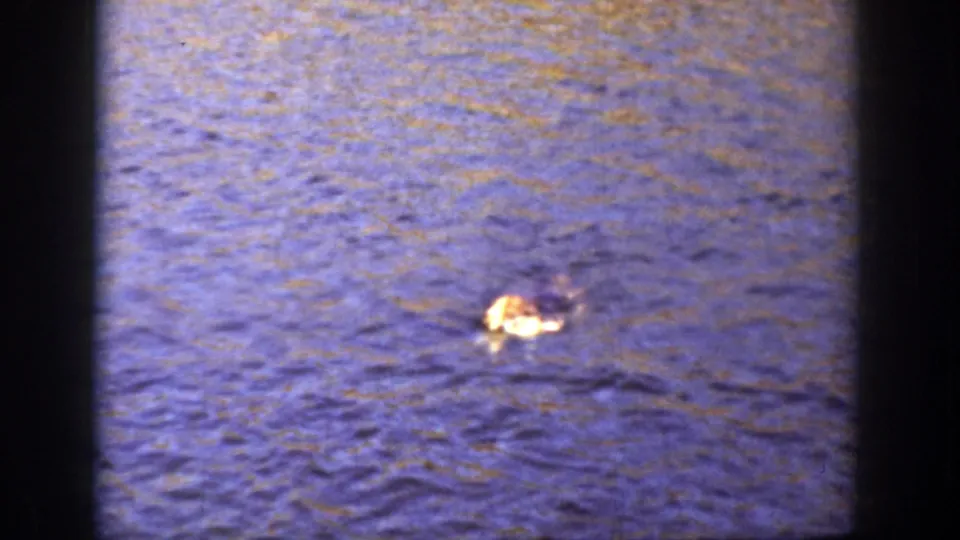 1936 California home-movie frame showing a light-and-dark floating object on rippling water with dark gate edges and visible film texture.