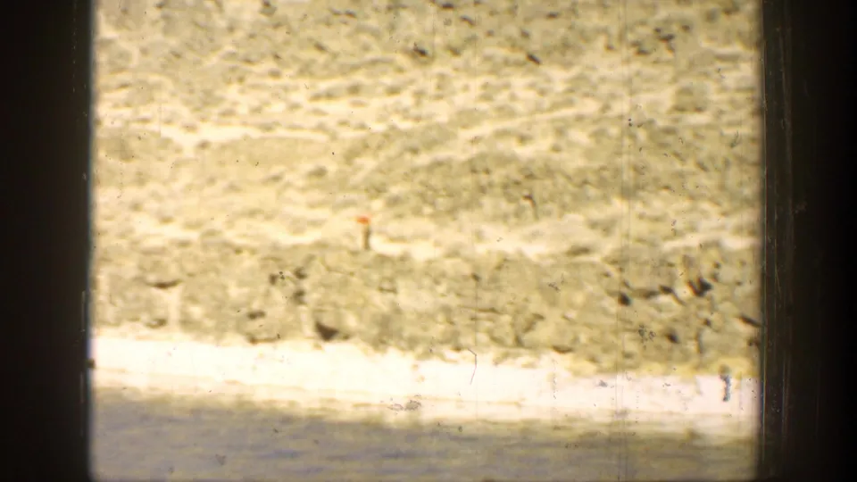 1936 California lakeside home-movie frame with pale shore, calm water, dry hillside, and visible dust and frame marks from the film scan.