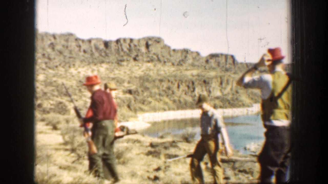 Several armed men stand and walk near water in rocky scrubland.