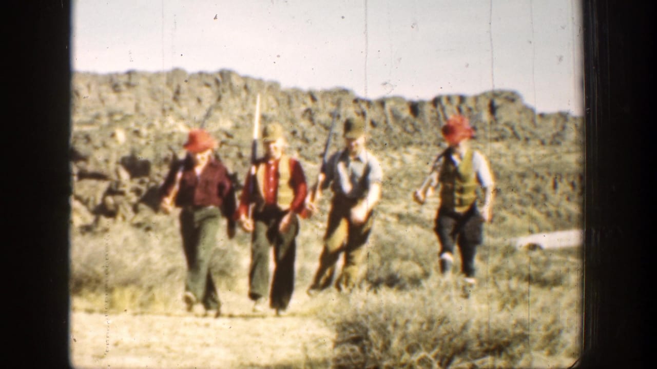 Four rifle-carrying men continue down a dusty path with hills and brush behind them.