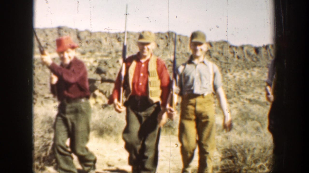 1936 California 8mm frame of men in caps and outdoor clothing walking across arid terrain with hunting rifles.