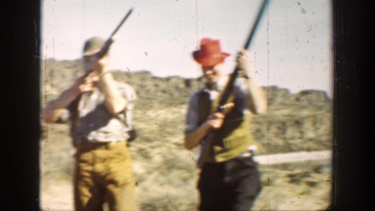 Two men stand or walk with long rifles in a dry open landscape.
