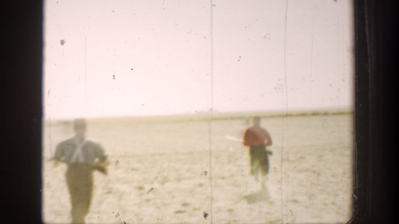 In 1936 California home-movie footage, two hunters run across sunlit arid ground under a pale sky.