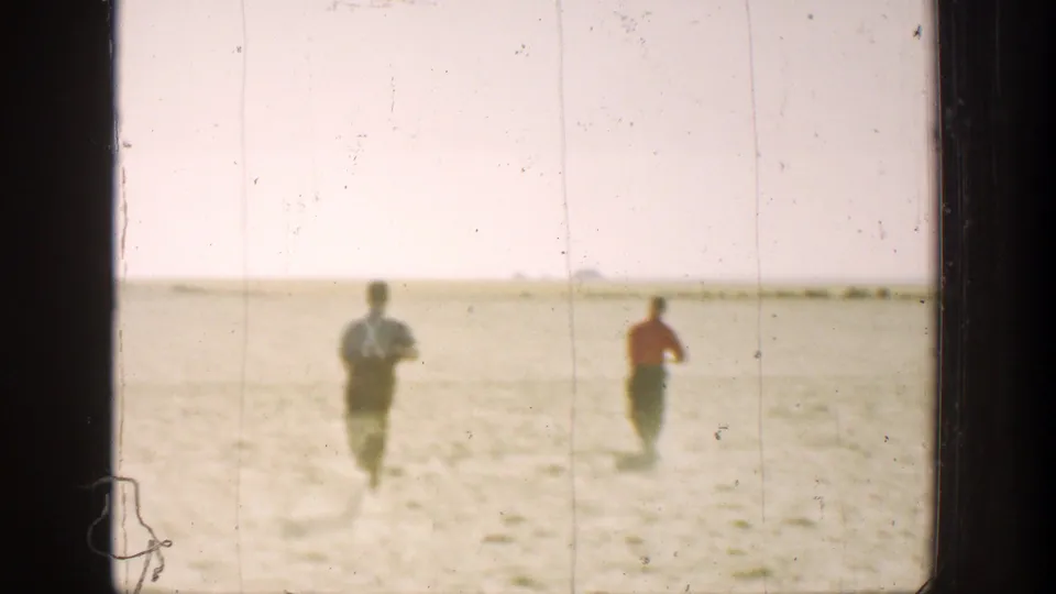 Two hunters continue running across a sun-washed California desert landscape in soft 8mm footage.