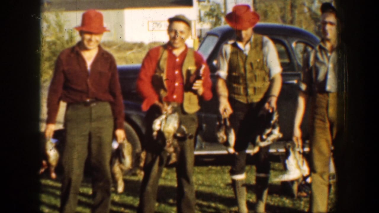 Men in red hats pose with harvested turkeys beside a dark vintage car.