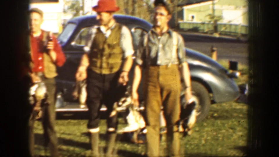 Three adult hunters, including one in a red hat and vest, hold harvested turkeys beside a dark 1930s car in California.