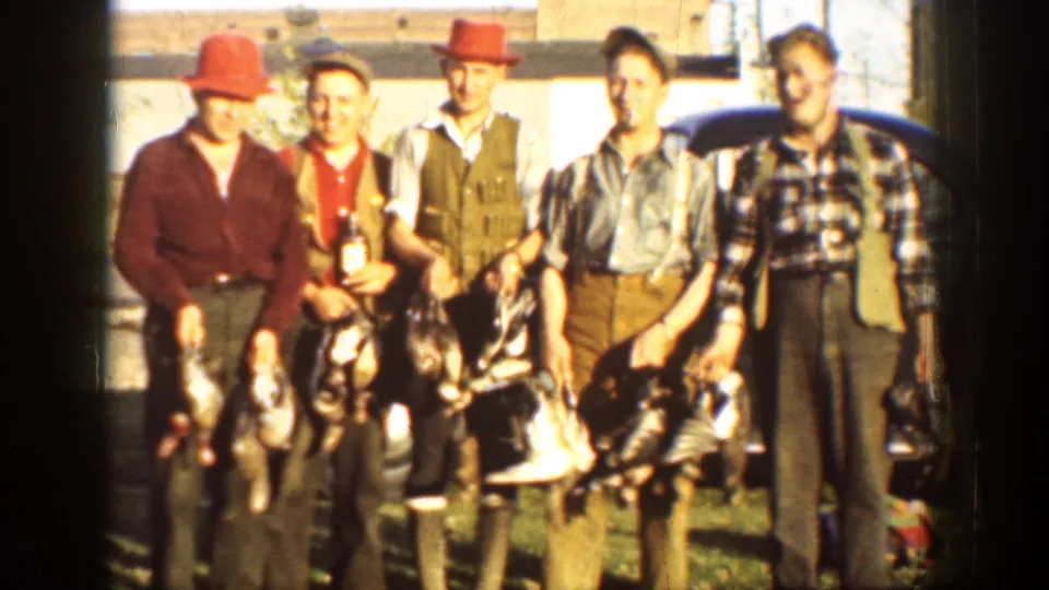 Four adult men pose with harvested turkeys near a dark 1930s automobile in a rural California home-movie scene.
