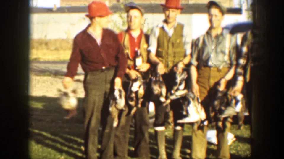 Several adult men in hunting clothes move or pose with ducks in a California outdoor home-movie frame.