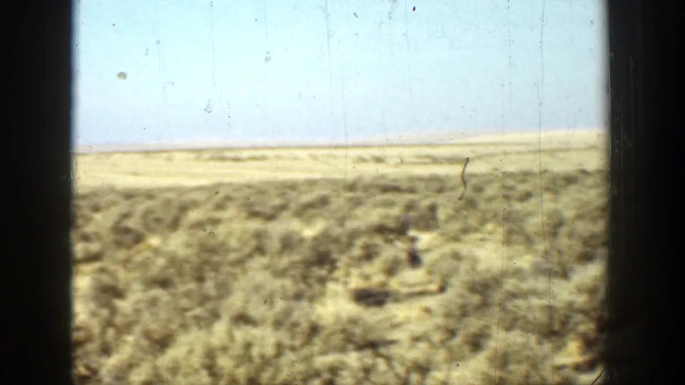 1936 California 8mm frame showing arid scrubland and a pale sky through dark window or gate edges.