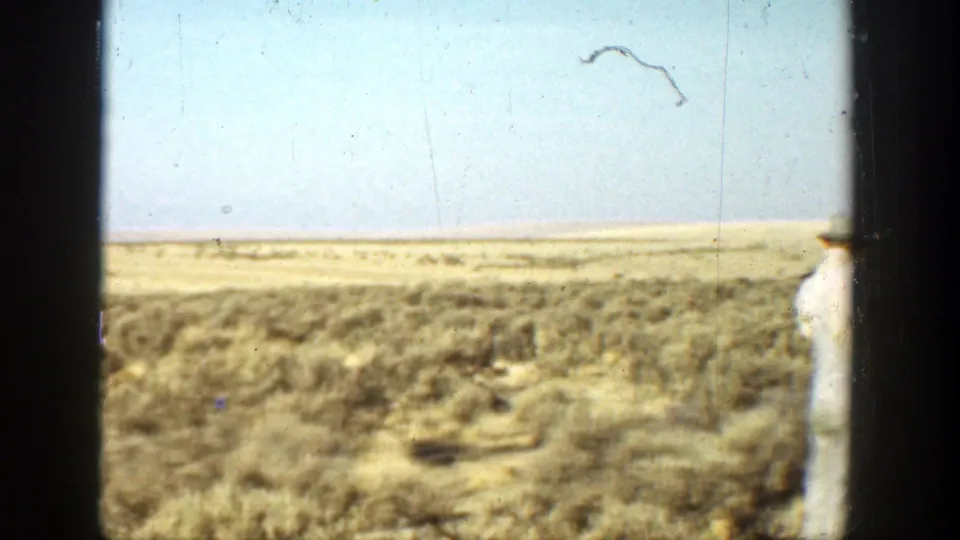 1936 California home-movie frame of dry open land with a light-clothed man partly visible at the right edge.