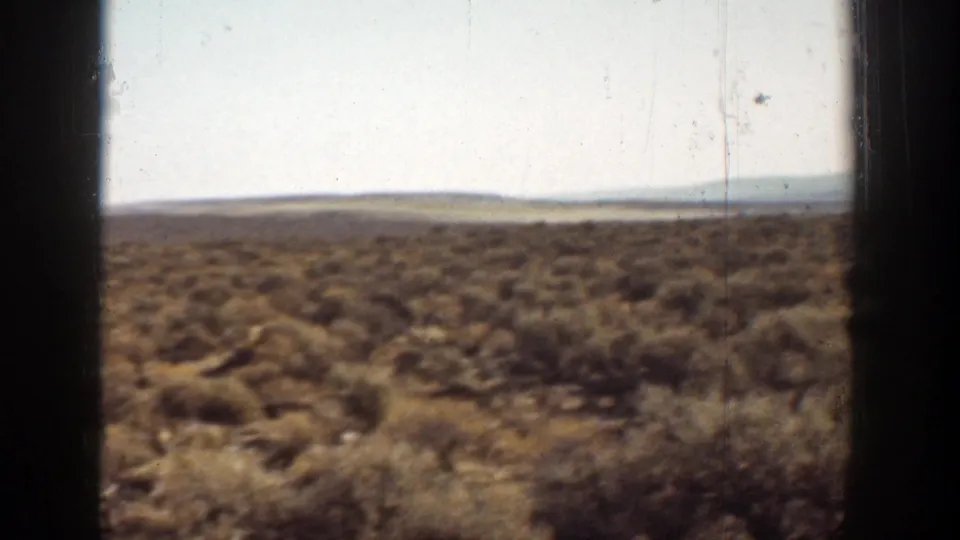 1936 California 8mm view of low brown desert shrubs, distant hills, and dark frame edges from a moving perspective.