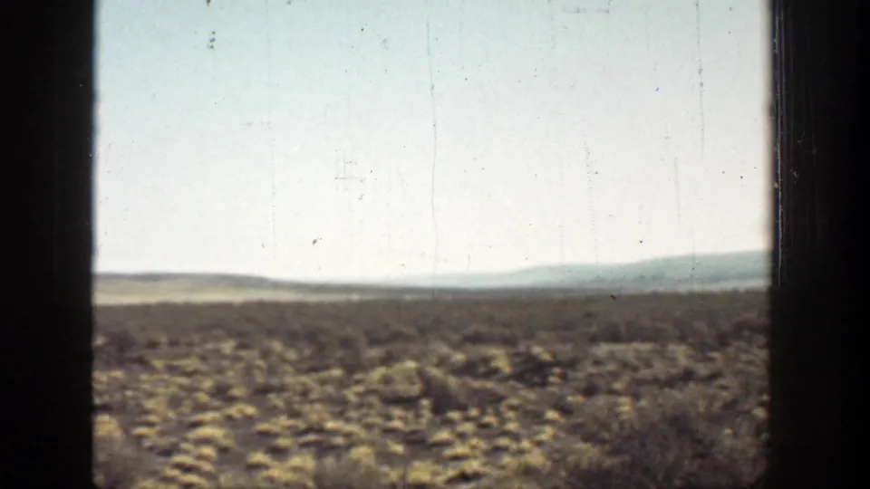 1936 California landscape frame with sparse desert vegetation, distant hills, gate shadowing, and visible film grain.