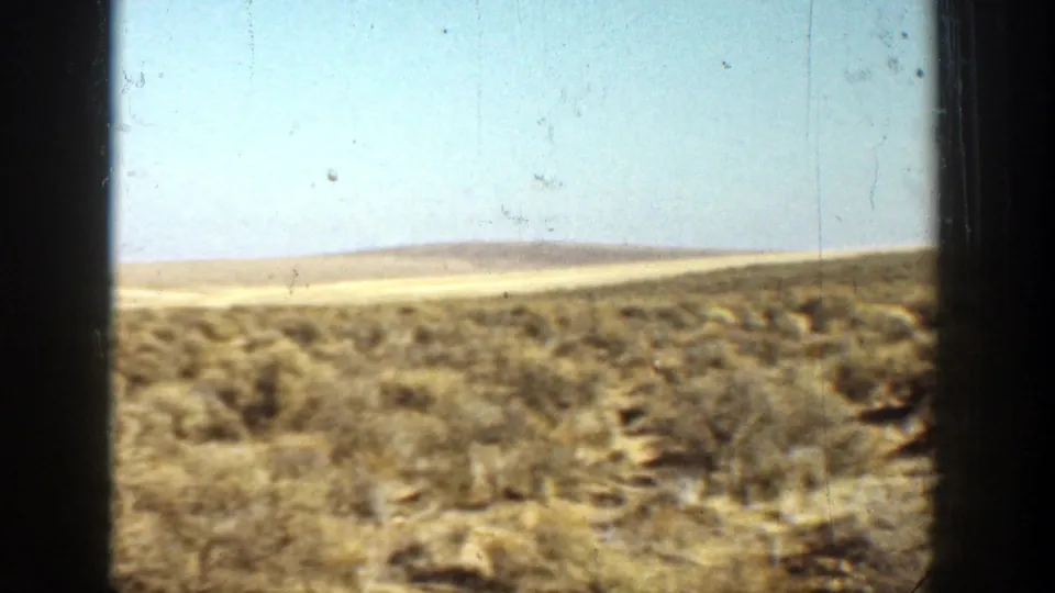The 1936 California home movie cuts to open desert scrubland and low hills beneath a bright, pale sky.