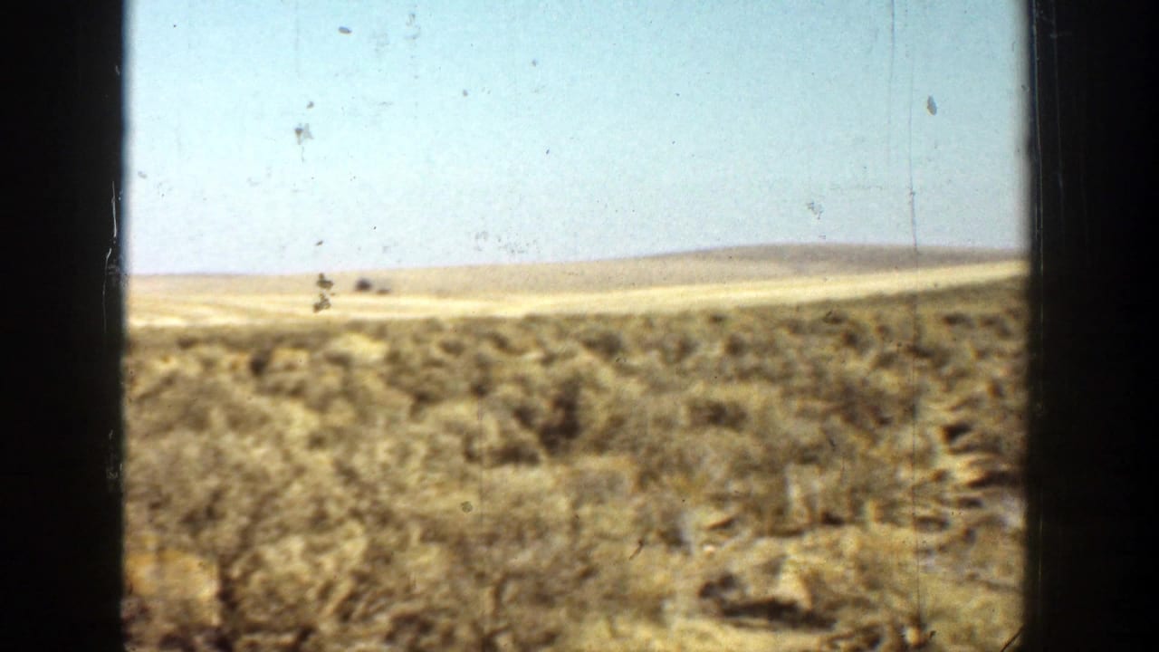 Dry scrub field and low hills seen through dark vertical film-frame edges.