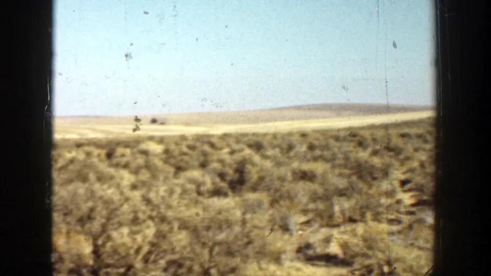 1936 California 8mm view of dry scrubland and distant low hills under a pale blue sky, framed by dark vertical edges.