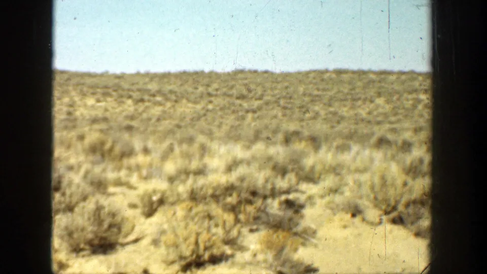1936 California home-movie frame showing an open brown field with sparse brush and a bright blue sky.