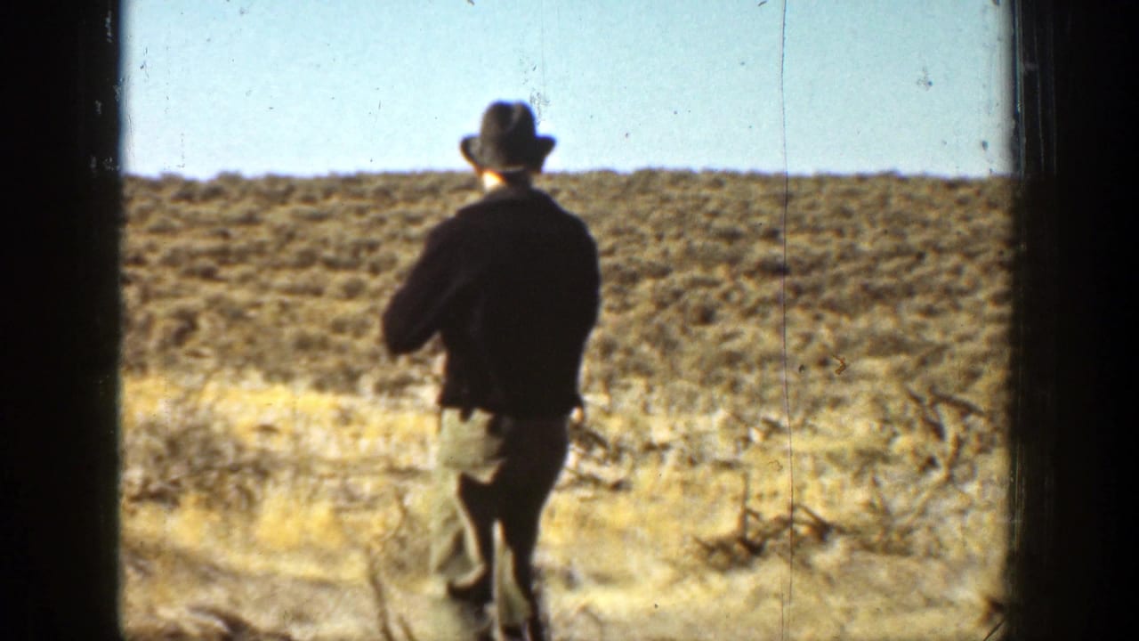 Man in a hat walks across dry scrubland seen through dark vertical frame edges.