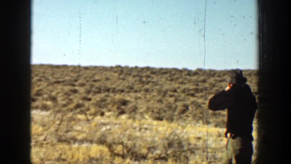 A man in a hat appears at the right of a dry California landscape, with dark window-like edges crossing the frame.