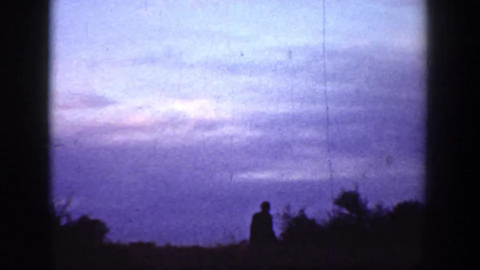 A silhouetted figure stands low in the frame against a purple dusk sky in 1936 California home-movie footage.