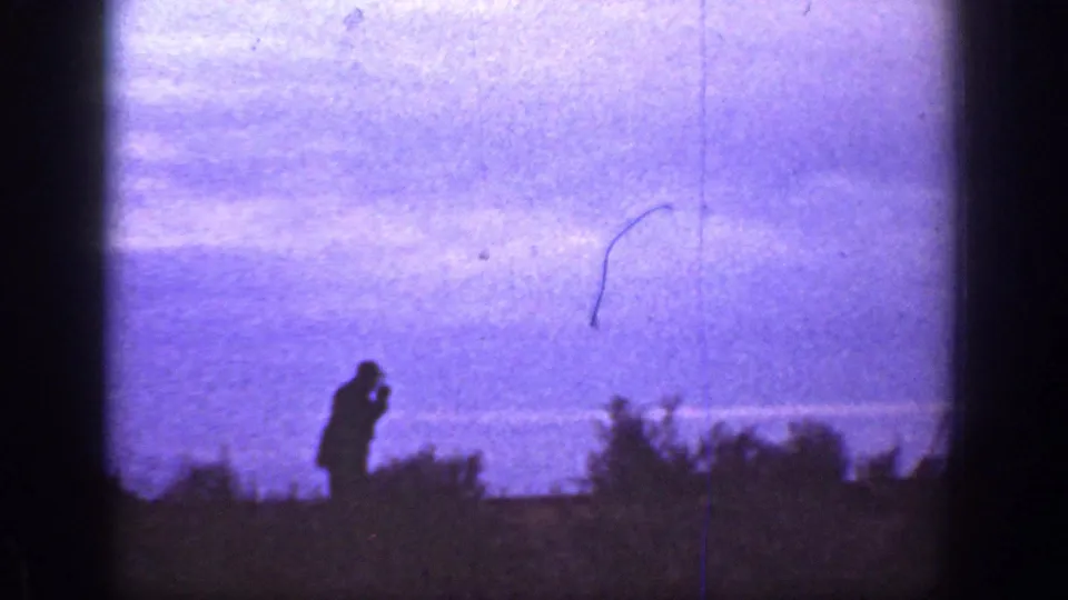 A hatted figure is silhouetted along a low scrub horizon under a purple dusk sky in California home-movie footage.