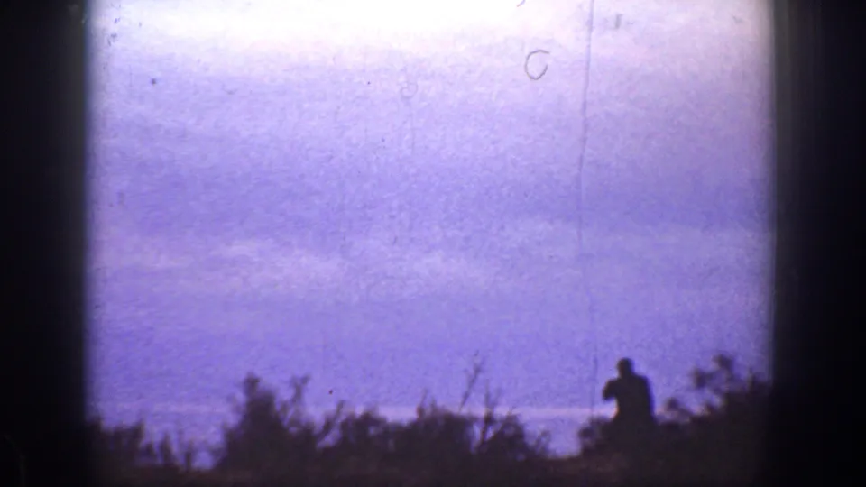 1936 California 8mm frame with a small dark figure near hillside brush, backed by a pale purple sky or water horizon.