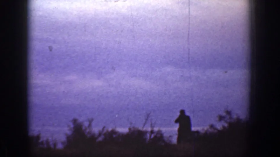 1936 California 8mm frame showing a lone silhouetted person near foreground vegetation and a bright purple-toned horizon.