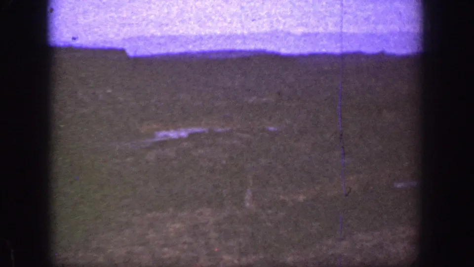 1936 California 8mm frame showing a dim grassy slope under a purple-tinted upper band, with scratches, grain, and dark gate edges.