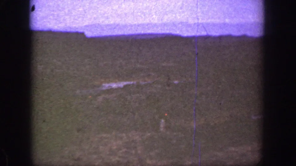 1936 California 8mm frame of a low-lit hillside with faint pale ground marks, purple color shift, grain, and vertical film lines.