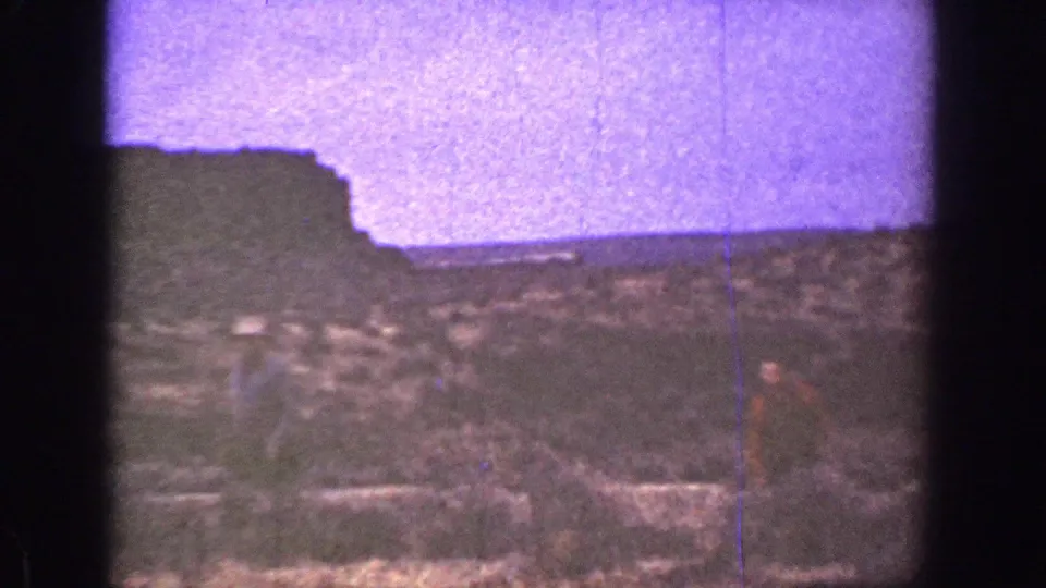 1936 California desert frame with one hat-wearing man more visible and another figure partly seen near low brush and rock.