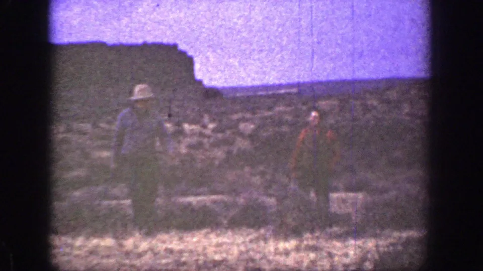 1936 California frame showing two hat-wearing men on rugged desert terrain, one holding an apparent long gun.