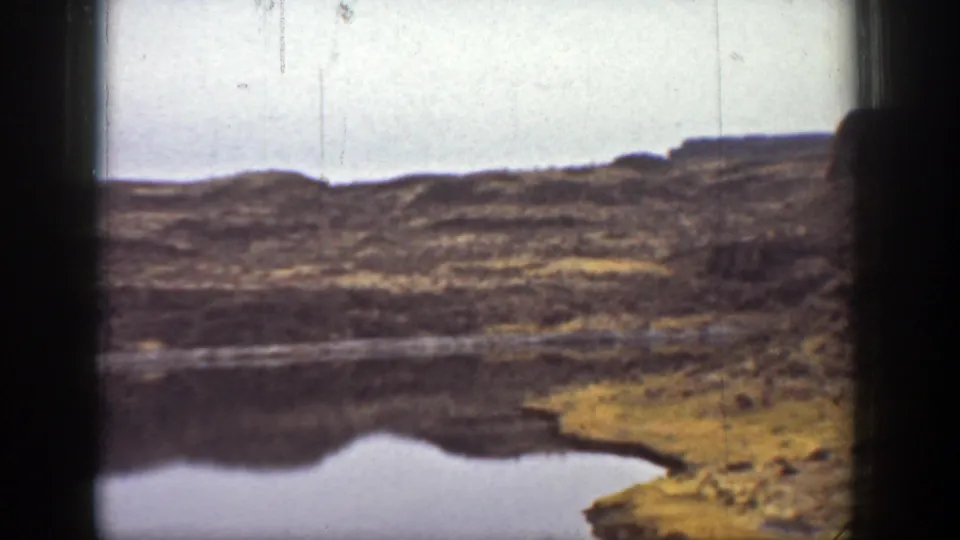 A small reflective pool appears in the dry California canyon landscape, with low ridges and brush beyond it.