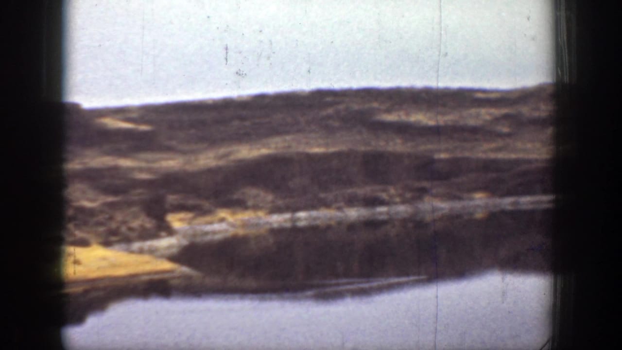 1936 California 8mm frame showing rolling dry hills and a small lake or reservoir with dark gate shadows at the sides.