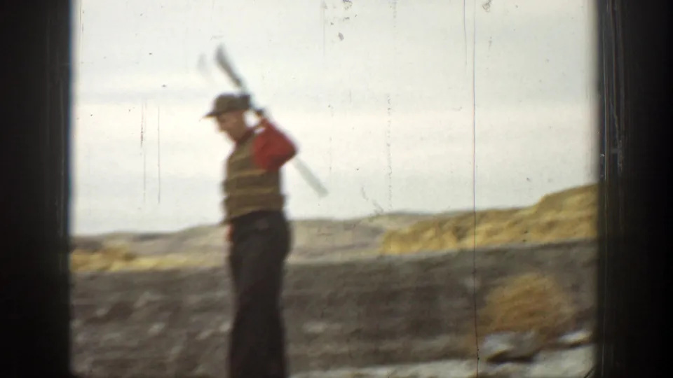 In 1936 California home-movie footage, a man in a red vest and cap stands with a long gun over his shoulder in an arid landscape.