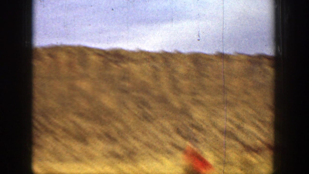 1936 California 8mm frame showing a dry hillside, pale sky, dark film borders, and a blurred red object or garment near the bottom edge.