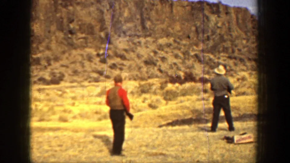 Two adult men in a dry California field in 1936, one wearing red and one in a light hat, with a rocky bluff behind them.