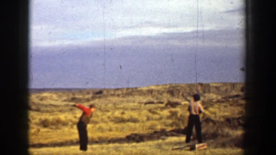 1936 California home-movie frame of two men in a dry open field, one in red and one in a light shirt, raising their arms during recreation.
