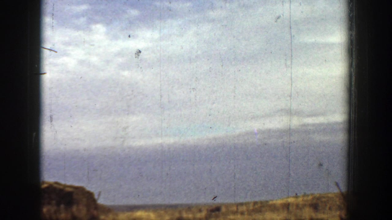 Open arid landscape with partial dark film-frame edges and distant hills.
