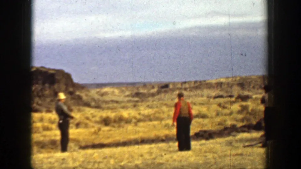 1936 California home-movie frame showing three adults on an open plain, one in a hat holding a rifle while others stand nearby.
