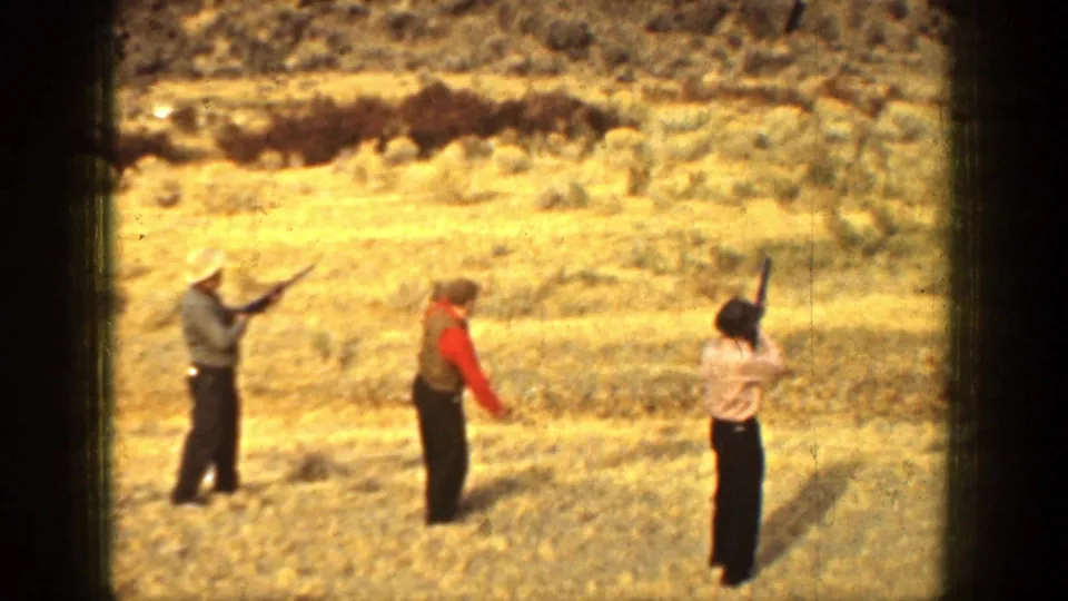 1936 California home-movie frame showing three adults with rifles positioned across an open arid field below low hills.