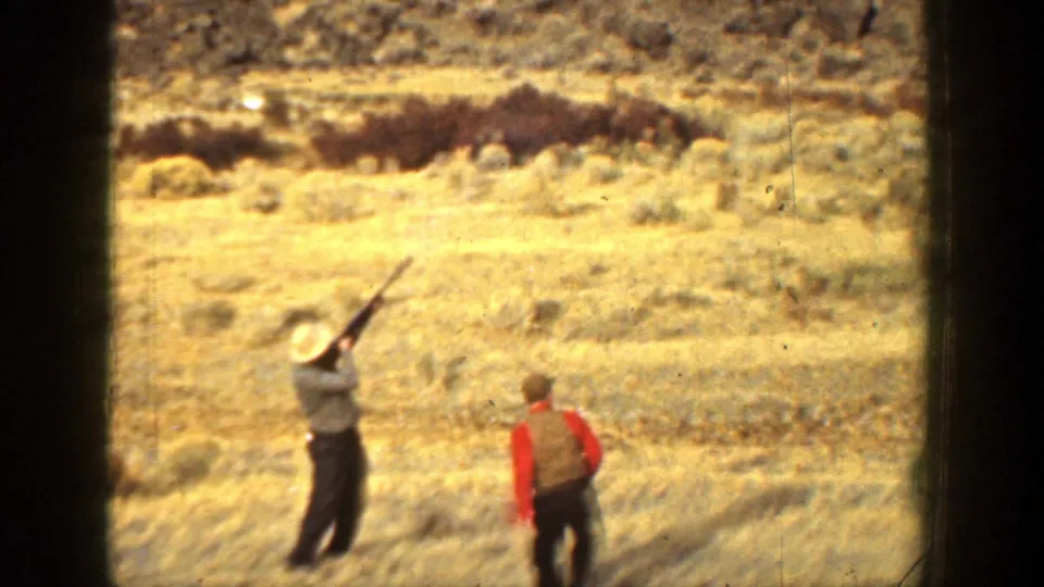 In the closing frame, one man in a hat aims a shotgun upward while another stands nearby in the dry California landscape.