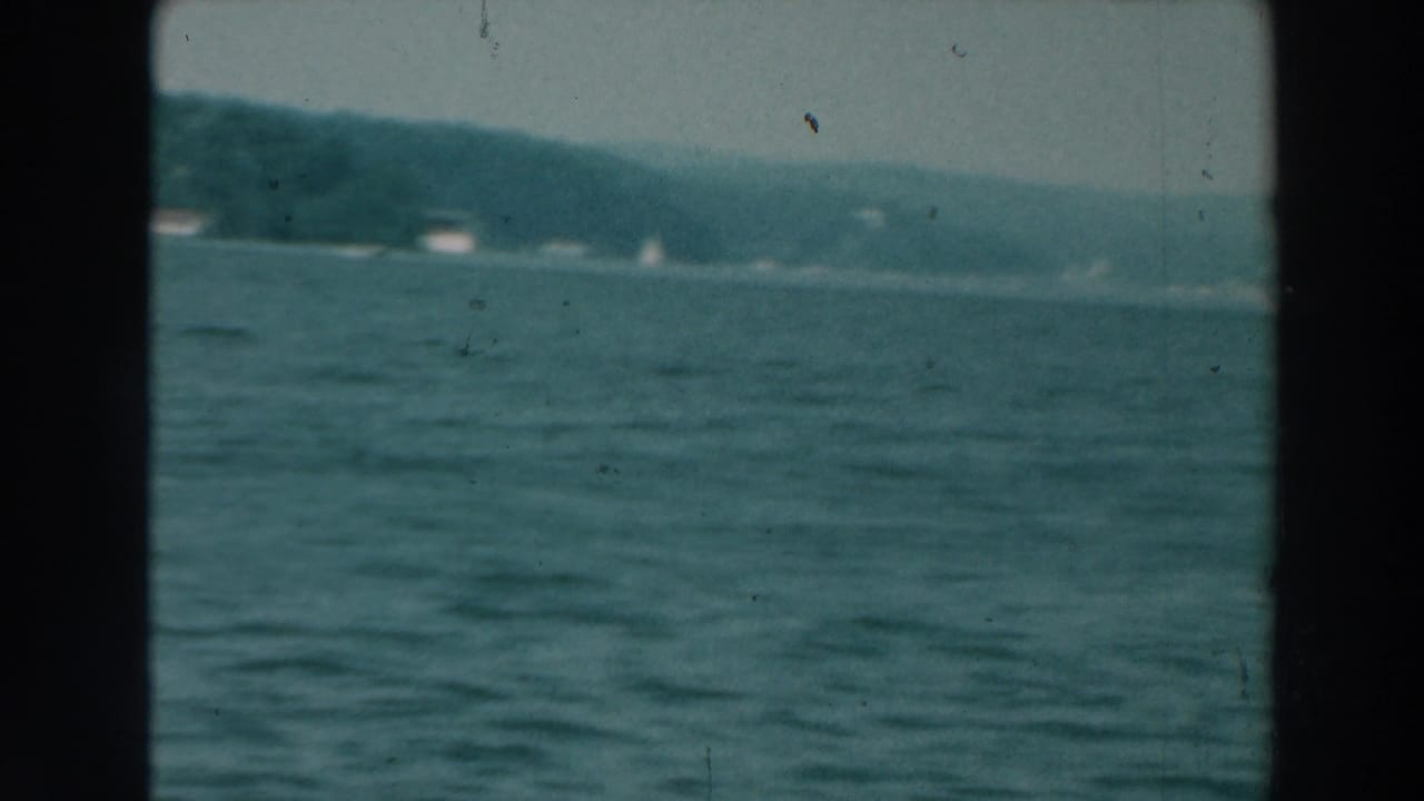 Open lake surface with a distant tree-lined shore and faint small boats near the horizon.