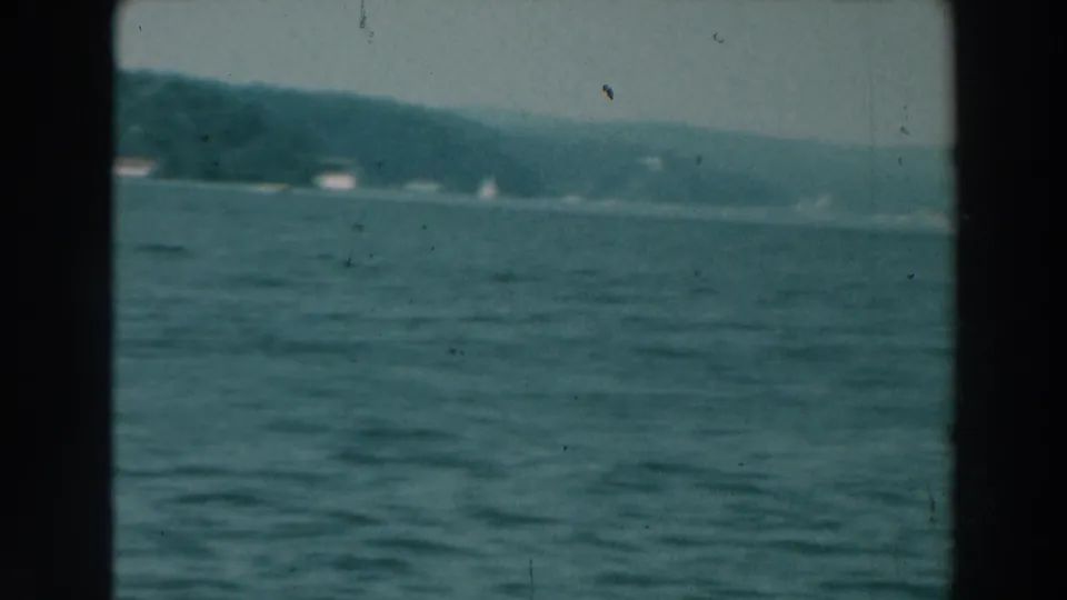 Lake Winnebago water fills the foreground while a hazy wooded shoreline and tiny distant boats sit near the horizon.