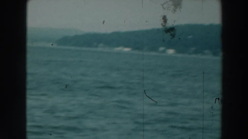 Soft 8mm frame of Lake Winnebago with textured water in front and a distant wooded shoreline with faint structures beyond.