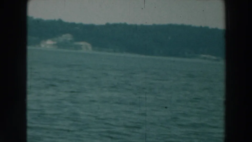 A late frame from the Lake Winnebago boat view shows rippled water, wooded banks and pale distant lakeside structures.
