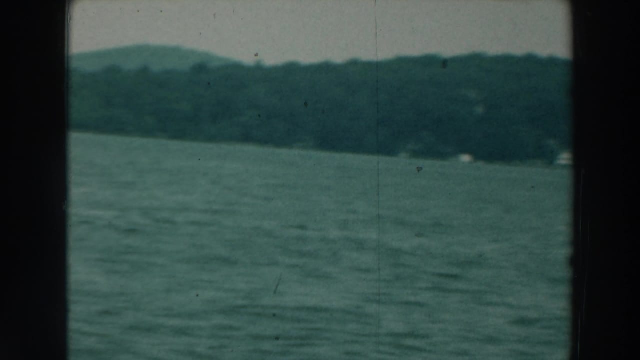 Wide lake surface with distant wooded hills or shoreline and dark vertical frame borders.