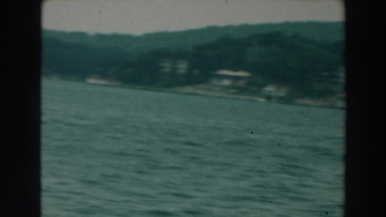Wide lake view with distant wooded shoreline and small houses.
