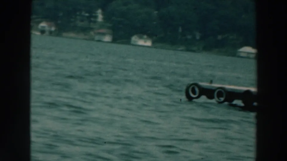 Lake Winnebago water and wooded shore, with distant houses and a tire-lined dock edge entering frame.