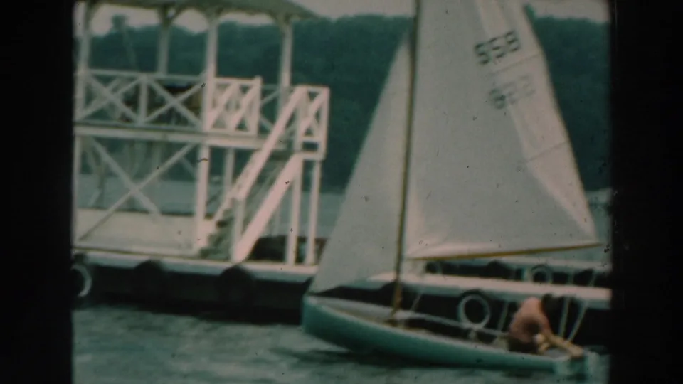 Small sailboat near a dock and white pier structure on Lake Winnebago in 1964 home-movie footage.