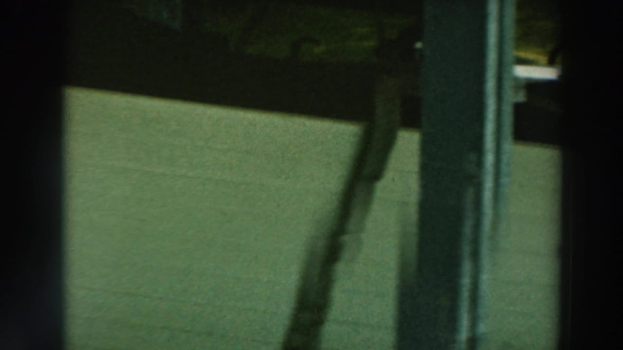 1964 Lake Winnebago 8mm frame showing a white boat hull stored beneath a wooden pier, partly obscured by vertical posts.